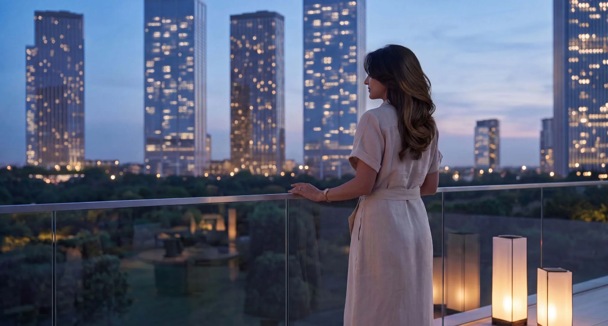 A resident on a private balcony at Valia at dusk, looking out over the landscaped podium and the lit towers of Dubai Creek Harbour